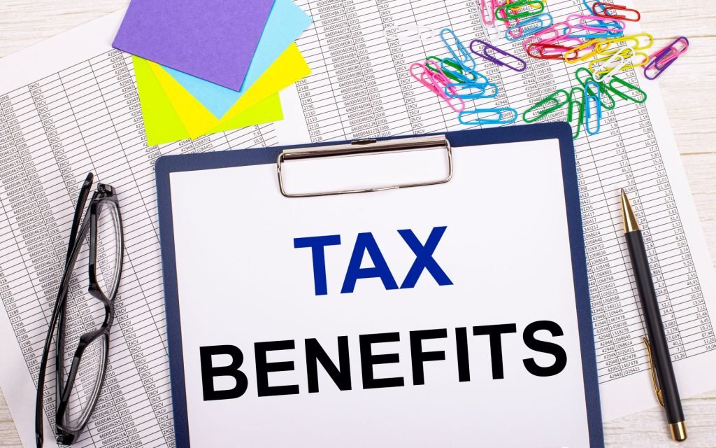 notepad with text tax benefits pen reports bright stickers paper clips glasses lie white office table top view with copy space flat lay