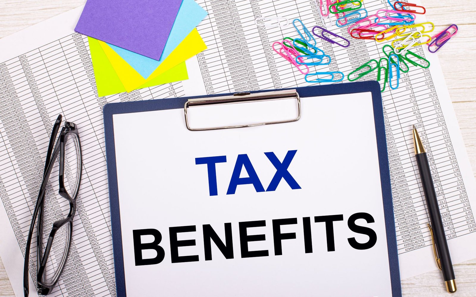 notepad with text tax benefits pen reports bright stickers paper clips glasses lie white office table top view with copy space flat lay